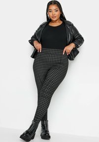 Chaqueta de cuero sintético negra, top negro ajustado y leggings con patrón de pata de gallo en tonos grises. Botines negros gruesos con cremalleras.