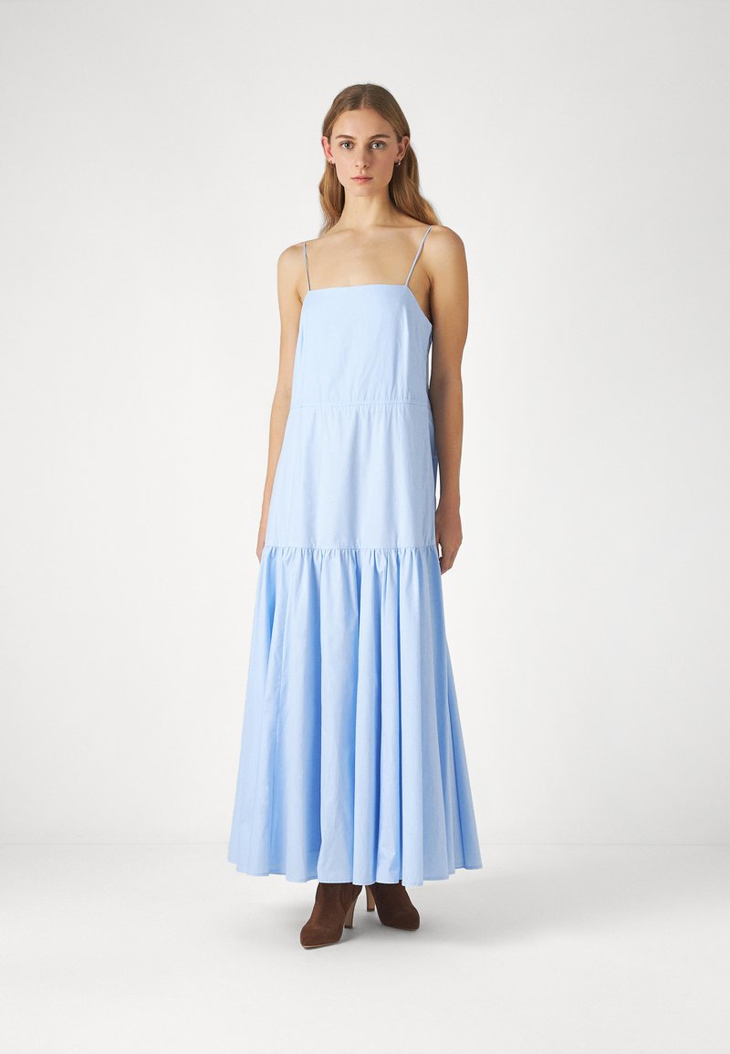Rochie lungă, de culoare albastră deschisă, din bumbac, cu bretele subțiri, un corset ajustat și o fustă în straturi. Accentuată cu o textură netedă și un design care ajunge până la podea.