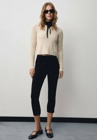 Crème fuzzy trui met een cropped ontwerp, gecombineerd met zwarte strakke broeken en zwarte enkelschoentjes. Model draagt een zonnebril.