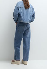 Světle modrá džínová bunda s padlými rameny a zkráceným střihem, v páru s vysokými modrými džíny. Look doplňují platformové sandály.