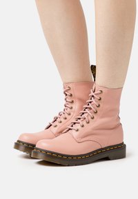 Pink leather lace-up ankle boots feature a round toe, gold eyelets, and a durable rubber sole with a contrasting yellow stitching detail.