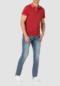 Rotes Polohemd mit Kragen und Knopfleiste mit drei Knöpfen, kombiniert mit hellblauen Jeans und weißen Sneakers. Lässige Kleidung aus Baumwollstoff.