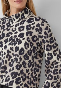 Maglia con collo a pipistrello realizzata in un tessuto beige con un motivo maculato nero, maniche lunghe e vestibilità comoda. Tessuto morbido.