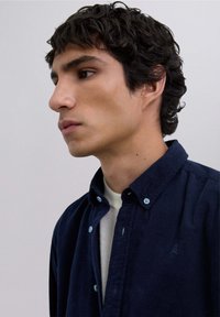 Camisa de botones de pana color navy con botones azul claro, un sutil detalle bordado en el pecho y un diseño de cuello clásico.