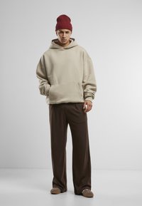 Haut à capuche beige surdimensionné avec poche avant et pantalon évasé marron. Porté avec un bonnet en tricot bordeaux et des chaussures décontractées marron clair.