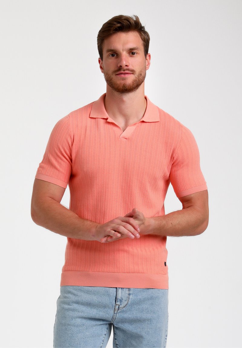 Polo tričko s krátkým rukávem v korálové barvě s texturou, plochým límcem a žebrovaným lemem. V kombinaci se světle modrými džíny.