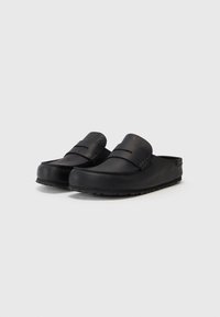 Mocassins noires à enfiler en matériau lisse avec un bout arrondi, des accents de couture et une semelle en caoutchouc texturée.