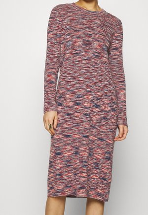 Femme portant une robe ajustée à manches longues, arrivant au genou, avec un motif mauvigné multicolore en rouge, rose et bleu.