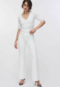 Haut en maille blanc à col en V et manches courtes, associé à un pantalon évasé blanc. Style avec des sandales à talons hauts noires à fines lanières.