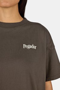 Hnedé bavlnené tričko s okrúhlym výstrihom a krátkymi rukávmi. Na ľavej strane hrude sa nachádza biele logo "Pegador".