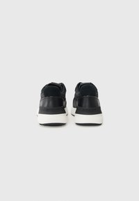 Sorte joggesko med en teksturert stoffoverdel, glatte lærdetaljer og en hvit gummisåle. Har et minimalistisk design.