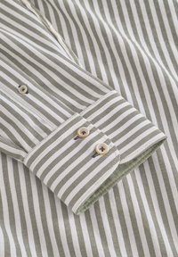 Polsino di camicia a righe verdi e bianche con due aperture per bottoni, caratterizzato da un tessuto interno verde a contrasto e una texture fine.