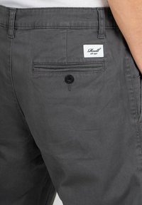 Graue Baumwollhose mit einer Gesäßtasche, die über einen Knopfverschluss und ein markiertes Etikett verfügt. Sanfte Textur und klassisches Schnittdesign.