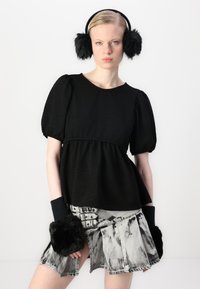 Top nero con texture, maniche a sbuffo e vita a peplo; abbinato a pantaloni grigi con motivo tie-dye e accenti in pelliccia nera sui scaldamani.