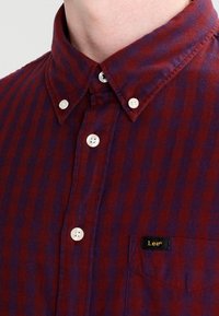 Camicia a righe rossa e viola con colletto a punte, bottoni bianchi e taschino sul petto sinistro con etichetta nera "Lee".