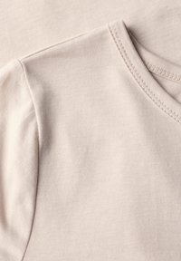 Camiseta de algodón en beis claro, con cuello redondo, mangas cortas y una sutil textura acanalada con detalles de costura.