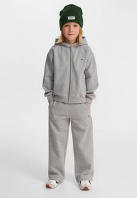 Szara bluza z kapturem i dopasowane spodnie dresowe wykonane z miękkiego materiału, w zestawie z zieloną czapką typu beanie. Posiadają zapięcie na zamek błyskawiczny oraz akcenty z logo.