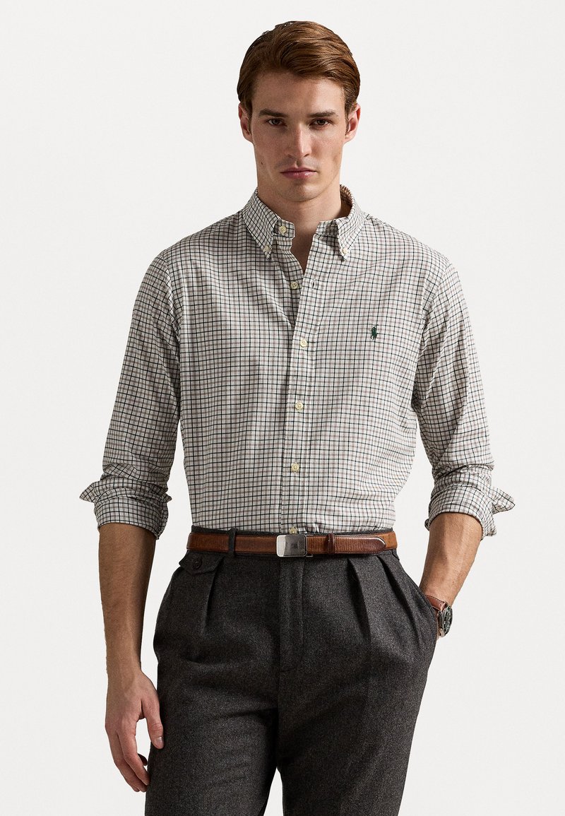 Skjorte med knappelukking og et lite rutemønster i hvitt og mørkebrunt, med oppbrettede ermer og en grønn logo på brystet.