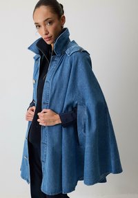 Denim kappefrakke i lys blå, med høj krave, trykknapper og sidelommer. Løs pasform med et svajende design.
