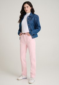 Giacca di jeans blu, dolcevita bianco, pantaloni rosa e scarpe da ginnastica bianche. La giacca presenta una chiusura con bottoni e tasche; i pantaloni hanno una cintura.