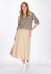 Robe en coton beige avec une finition texturée, associée à un pull en tricot rayé marron et beige et des baskets montantes blanches.