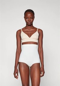 Μπεζ μπραλέτα με λεπτές τιράντες και σχέδιο V, συνδυασμένη με λευκά ψηλόμεσα σλιπ. Ομαλή υφή, μινιμαλιστικό στυλ.