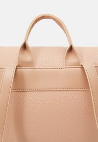 Sac à main en cuir de couleur pêche avec une finition texturée, présentant deux poignées supérieures et des accents de couture horizontale.