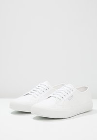 Vita canvas sneakers med rund form, snörning fram, strukturerad sula och subtil logotypdetalj på sidan. Slät finish över hela skon.