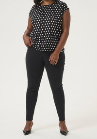 Haut noir à pois avec des manches courtes, associé à un jean skinny noir. Tissu texturé et finition lisse. Talons avec accents de nœud.