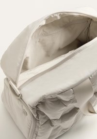 Világos bézs színű steppelt hátizsák felső cipzárral, belső zsebbel és textil pántokkal. Puha tapintású, strukturált formájú és minimalista kialakítású.