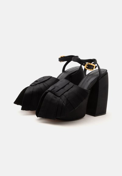 Sandales compensées à talons hauts noires avec brides à la cheville, boucles dorées et larges bandes plissées en satin sur les orteils.
