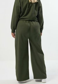 Grön oversized sweatshirt med löst sittande byxor, som har elastisk midja och en mjuk, slät struktur. Minimalistisk design och vida ben.