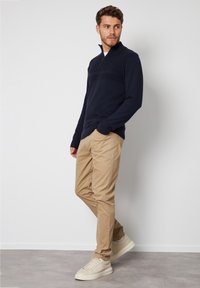 Marineblauer Reißverschluss-Pullover mit geripptem Design auf der Brust, kombiniert mit khakifarbenen Chinos und beigen Sneakers. Das Outfit hat eine lockere Passform und klare Linien.