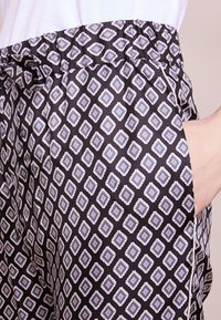 Černé vzorované kalhoty s diamantovým designem v modré a krémové barvě. Mají elastický pas a boční kapsy. Hladká textura.