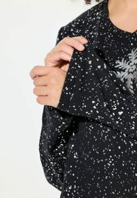 Top nero con un motivo a macchie argento, caratterizzato da un collo rotondo e maniche lunghe. Texture morbida visibile nei dettagli del tessuto.