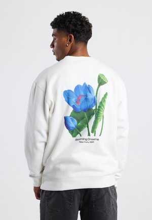 White sweatshirt featuring a vibrant blue floral graphic on the back, along with green leaves and text "Blooming Dreams, New York, 1989."