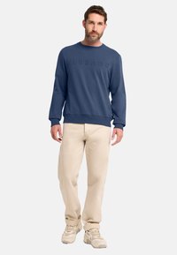 Marineblaue Sweatshirt mit erhabenem Text, Rundhals, gerippten Bündchen und Saum. Kombiniert mit beigen Hosen und hellen Sneakers.