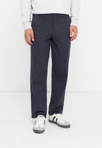 Navy blue cotton trousers with a straight leg fit, button closure, and belt loops, paired with gray and white athletic sneakers.