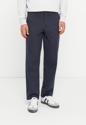 Navy blue cotton trousers with a straight leg fit, button closure, and belt loops, paired with gray and white athletic sneakers.