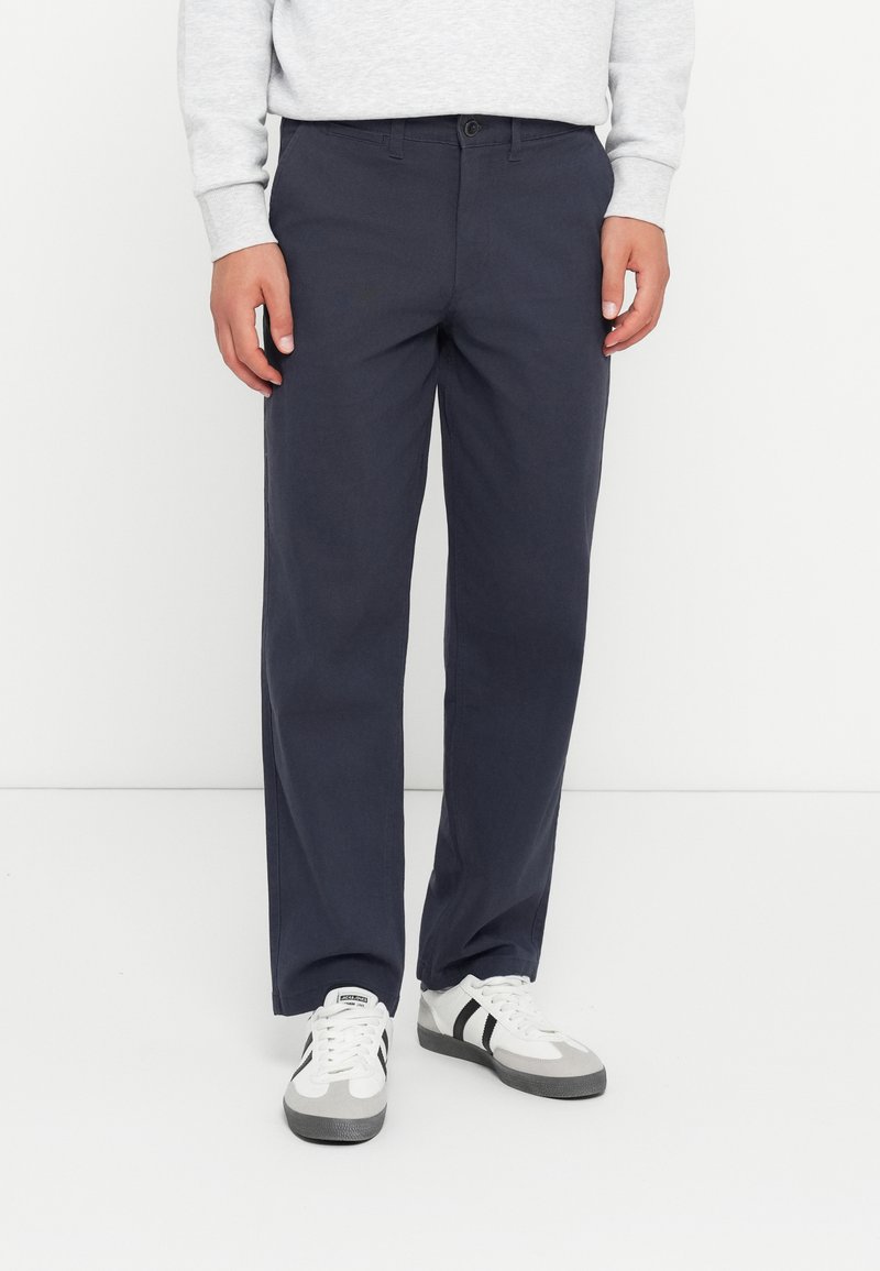 Navy blue cotton trousers with a straight leg fit, button closure, and belt loops, paired with gray and white athletic sneakers.