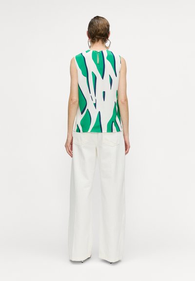 Top sin mangas en blanco con patrones abstractos en verde y azul marino. Presenta un escote en forma de llave en la parte posterior y se combina con pantalones de pierna ancha en un color blanco roto.