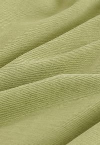 Tissu en coton vert clair avec texture de tissage visible, présenté en plis doux mettant en valeur un matériau lisse et respirant.