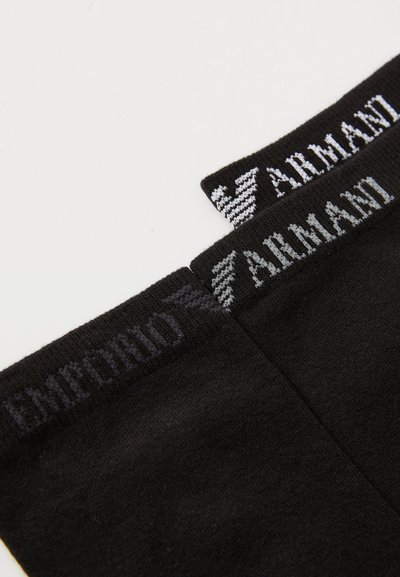 Melni zeķes ar kontrastējošu logo ribotajā aprocē; uzraksti "Emporio" un "Armani" baltā un pelēkā krāsā. Gluda tekstūra, vienkāršs dizains.