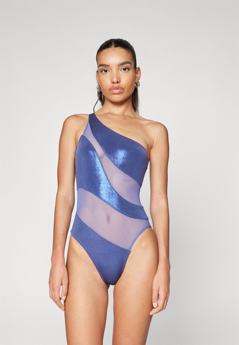 Maillot de bain une pièce avec un design diagonal à une épaule. Fabriqué en tissu bleu pailleté avec des sections transparentes, créant un motif ondulé.