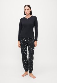 Top negru cu mâneci lungi și decolteu în V, împreună cu pantaloni de pijama elastici negri cu buline albe. Material moale, cu o croială confortabilă.