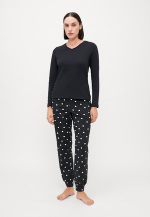 Zwarte lange mouw top met een V-hals en elastische zwarte pyjamabroek met witte stippen. Zacht materiaal met een relaxte pasvorm.