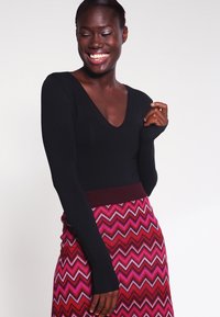 Top nero a maniche lunghe con scollo a V abbinato a una gonna a zigzag nei colori rosa e rosso, con una vita a coste.