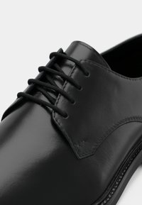 Μαύρο δερμάτινο παπούτσι φόρεμα με λείο, γυαλιστερό φινίρισμα, που διαθέτει έξι οπές, στρογγυλά μαύρα κορδόνια και διακριτές ραφές στην επάνω πλευρά.