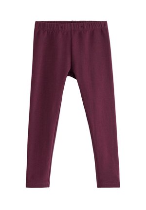 Barn med krøllet hår iført en mørkerød sweatshirt, leggings og mørkerøde sneakers, står på ét ben mod en ensfarvet hvid baggrund.