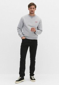 Szary sweatshirt z okrągłym dekoltem i małym czerwonym logo, w połączeniu z czarnymi dżinsami i czarnymi trampkami z białymi podeszwami. Prosty design, swobodny krój.